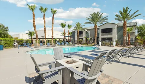 Millennium East Apartments community pool lounge area showing pool chairs and entrance to building and palm trees in the background